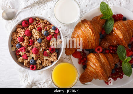 Sana colazione: muesli con frutti di bosco e croissant, latte e succo di arancia vicino sul tavolo. vista orizzontale dal di sopra Foto Stock