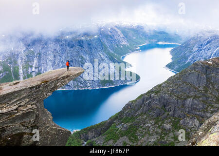 Escursionista femmina permanente sulla Trolltunga (troll lingua) famosa roccia alta al di sopra di un lago con vista panoramica della valle, popolare avventura turistica trek Foto Stock