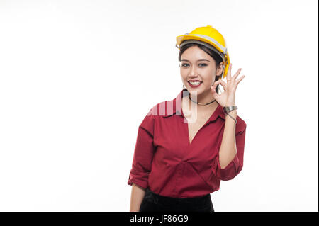 Donna asiatica ingegnere in maglietta rossa e gialla cappuccio di sicurezza rendendo bene l'azione. Persone gesticolando in business e concetto enginerring Foto Stock