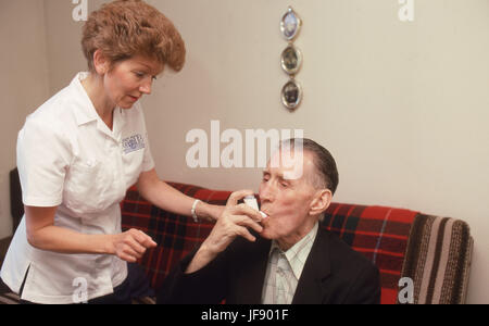 Visitatore di salute assistere uomo anziano con il suo farmaco di asma in alloggi protetti Foto Stock