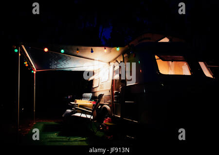 Vintage retrò camping trailer di notte nella natura della Francia con luci colorate e sedie Foto Stock