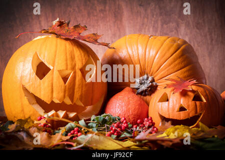 Zucche di Halloween, scolpiti jack-o-lantern in caduta foglie. Sfondo di legno Foto Stock