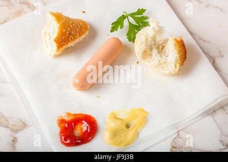 Mangiare salsicce (Frankfurter) su carta con pane, senape e ketchup Foto Stock