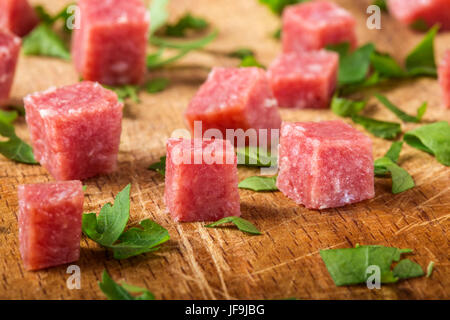 Close-up di piccoli cubetti di affumicato salame italiano sul tagliere di legno Foto Stock