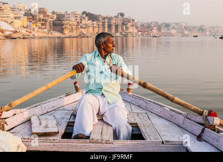 Un uomo indiano remare una barca per escursioni sul fiume Gange, Varanasi (India). Foto Stock