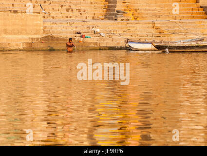 Un uomo la balneazione nelle acque del fiume Gange al di sotto di un ghat di Varanasi, Uttar Pradesh, India. Foto Stock