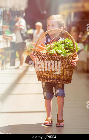 Ragazzo con cesto di frutta e verdura. Un bambino è in possesso di un cestello nel mercato. Foto Stock