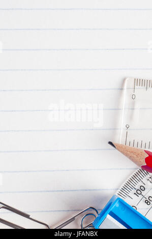 Una selezione di articoli di cancelleria confinanti con il fondo e il lato destro di una carta rigata sfondo da una scuola esercizio libro. Foto Stock