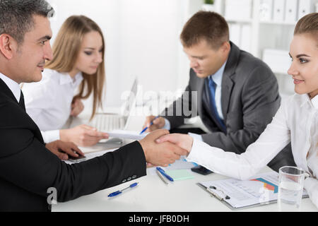 Imprenditore in abito donna agitando la mano con i loro colleghi che agiscono in background. Partner Deal realizzati e sigillato con handclasp. Saluto formale Foto Stock