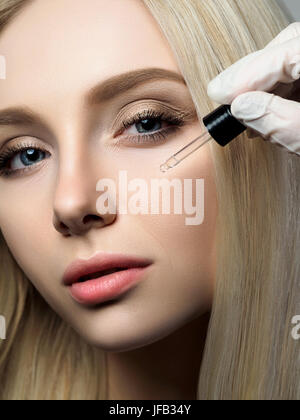Ritratto di bella donna bionda in bellezza. Cosmetologo applicando gocce di bellezza. Cura della pelle di lusso, estetista e per la cura della pelle del concetto. Foto Stock