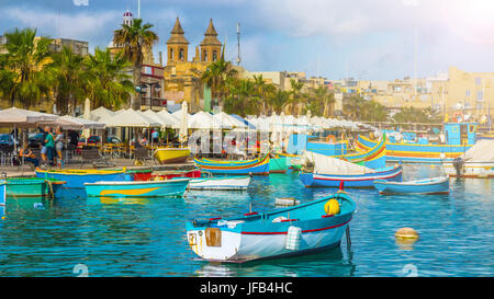 Marsaxlokk, Malta - tradizionale colorato Luzzu maltese fisherboat al vecchio villaggio di Marsaxlokk con acqua del mare turchese e palme su un estate Foto Stock