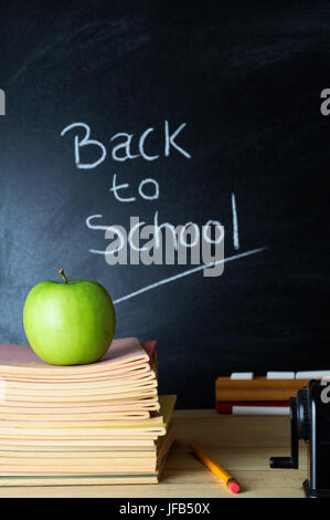 Insegnante di scrivania con una pila di libri, un apple e altre apparecchiature. Le parole "Si torna a scuola", scritto in gesso su una lavagna nella soft focus backgr Foto Stock