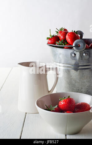 Un tavolo rustico scena di appena raccolto le fragole appena raccolte. Include un secchio di stagno di fragole, una crema brocca e una ciotola di servita strawbe Foto Stock