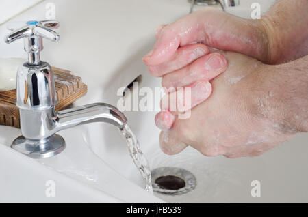 Mani maschio essendo lavato nella vecchia Cina lavandino con acqua in esecuzione in acciaio inossidabile tocca, e di una barra di sapone in appoggio su una tavola di legno portasapone. Foto Stock