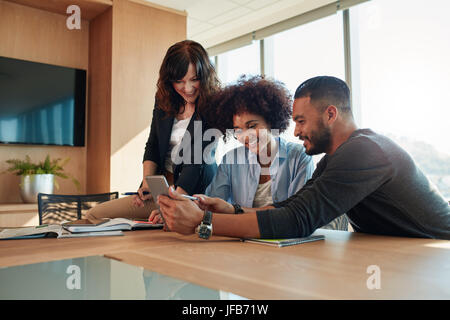 Gruppo di diversi imprenditori seduti insieme in ufficio e con tavoletta digitale. I giovani all'avvio utilizzando computer tablet e sorridente. Foto Stock