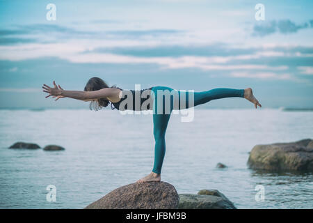 Giovane donna attraente la pratica dello yoga, in piedi nella posizione del Guerriero i tre esercizi, Virabhadrasana III pongono Foto Stock