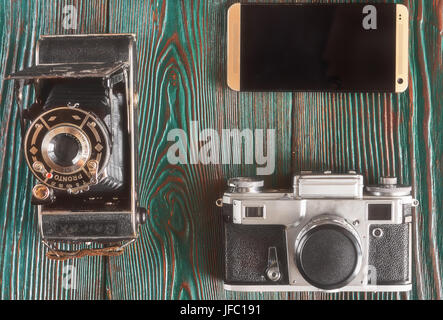 Tre generazioni di macchine fotografiche e vecchie foto sulla memoria. Antico autentico sfondo di legno. Foto Stock