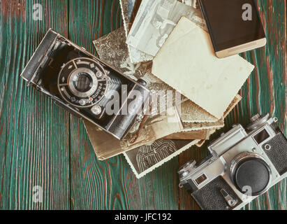 Tre generazioni di macchine fotografiche e vecchie foto sulla memoria. Antico autentico sfondo di legno. Foto Stock