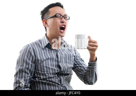 Sbadigliare maschio asiatico titolari di una tazza di caffè isolato su sfondo bianco Foto Stock