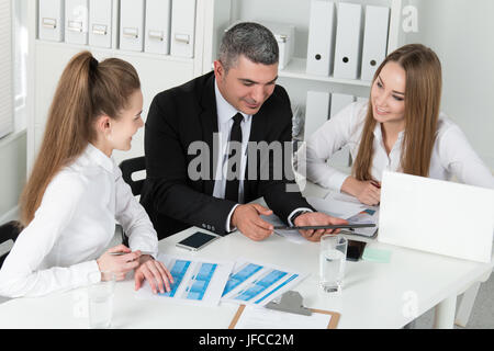 Imprenditore adulti consultando il suo giovane femmina i colleghi durante la riunione di affari. Partner documenti di discussione e idee Foto Stock