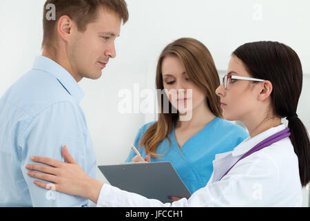 Gentile Dottore femmina maschio toccante braccio del paziente per l'incoraggiamento e l'empatia con la sua balia collega in background. Il partenariato, fiducia e medica Foto Stock