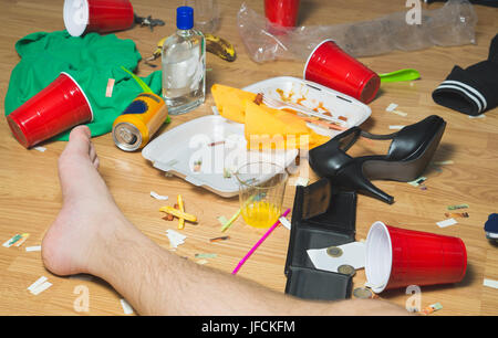 Appeso sopra l uomo ha passato fuori sul pavimento accanto al giorno per un partito, piede visibili. Cestino, gli avanzi di cibo, vestiti, tacchi alti e bottiglie in disordine home. Foto Stock