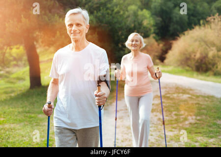 Stato d'animo positivo. Bello allegro uomo anziano holding Nordic walking e sorridenti mentre sono in uno stato d'animo positivo Foto Stock