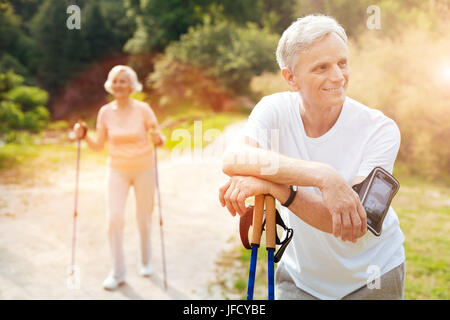 Il tempo di riposo. Felice felice allegro uomo appoggiata sul walking e sorridente durante il riposo dopo l'allenamento Foto Stock