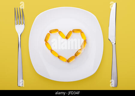 Olio di pesce gel morbidi giacente su bianco piastra di porcellana a forma di cuore (sfondo giallo) Foto Stock