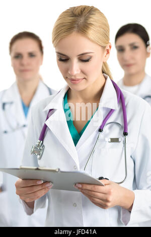 Ritratto di giovane biondo medico donna circondata da team medico, guardando il file con i documenti. La sanità e la medicina del concetto. Foto Stock
