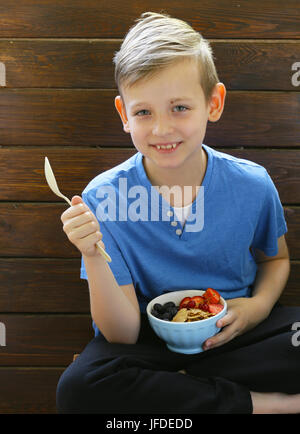 Il ragazzo ha una sana colazione a base di formaggio fresco e granola con frutti di bosco Foto Stock