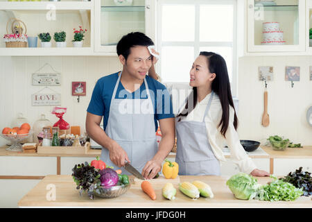 Asian giovane e bella moglie aiutando il marito asciugare il sudore fuori il suo volto nella cucina di casa. Felice amore giovane concetto. Foto Stock