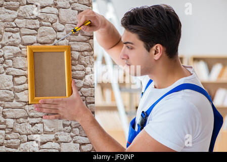 Repairman mettendo cornice immagine sulla parete Foto Stock