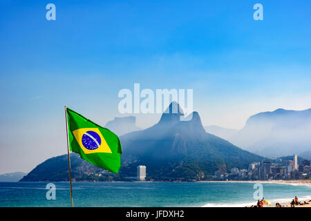 Bandiera brasiliana presso la spiaggia di Ipanema a Rio de Janeiro con due fratelli hill e pietra Gavea in background Foto Stock