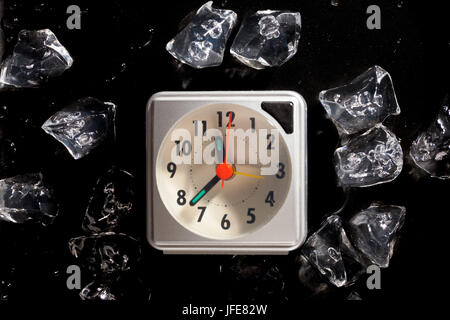 Congelati nel tempo concetto con cubetti di ghiaccio e di un orologio e di acqua di fusione scende su di uno sfondo scuro Foto Stock