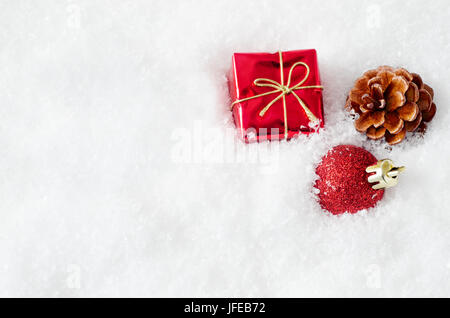 Un regalo di Natale scatola, pallina e cono di abete, incorporato in finto bianco della neve a destra del telaio, con copia spazio sulla sinistra. Foto Stock