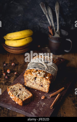 Pane alla banana con noci, cannella e scaglie di cioccolato sul tagliere di legno. Messa a fuoco selettiva. Alimentare la vita ancora, scuro foto Foto Stock