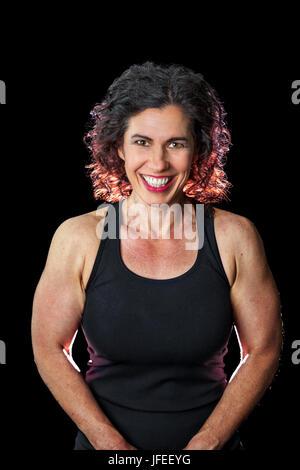Una buona ricerca weightlifter femmina sorrisi per la fotocamera. Ella è su sfondo nero ed è retroilluminato. Vi è un percorso per tagliare la donna fuori dal Foto Stock