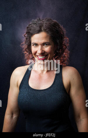 Ritratto di un sorridente, femmina weightlifter su uno sfondo nero. Ella è retroilluminato e non ci sono nuvole e le particelle di polvere di gesso galleggiante attraverso th Foto Stock