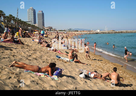 Una folla di persone a prendere il sole sulla spiaggia di Barceloneta; sullo sfondo i grattacieli Hotel Arts e Torre Mapfre, Vila Olimpica e Port Olimpic Foto Stock