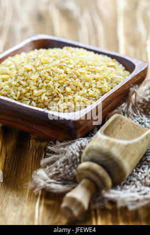 Non cotti bulgur in ciotola di legno e scoop. Foto Stock