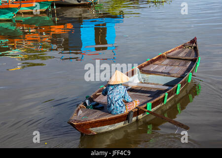 La donna in una barca a remi lookoing turistico per i clienti sul fiume Thu Bon in Hoi An, Vietnam Foto Stock