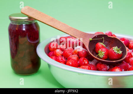 Le fragole dal produttore con lo zucchero e i vasetti per la produzione di marmellate su uno sfondo verde. Foto Stock