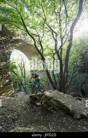 Uomo in sella moto su sentiero da arcuata di muro di pietra nella foresta Foto Stock