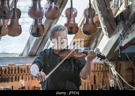 lavoratore che prova il violino in officina Foto Stock