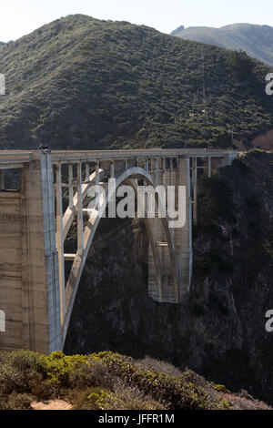 Parecchie persone sedute e gite turistiche in cima al Bixby Creek Bridge, un calcestruzzo, open-spandrel il ponte di arco, sulla Pacific Coast Highway. Foto Stock