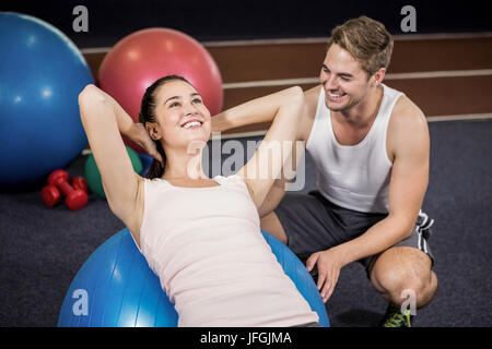 Il Trainer assiste una donna facendo sgranocchia addominale sulla sfera di fitness Foto Stock
