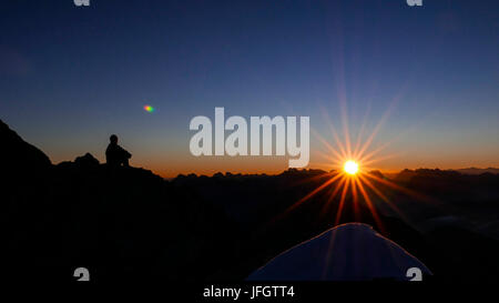 Alpinista ammira sunrise e sunray oltre Karwendel con Wörner e orientale punto di Karwendel e Birkkarspitze e Übersachallljoch e Bettelwurf, vista del Schüsselkarspitze nella gamma di Wetterstein, Foto Stock