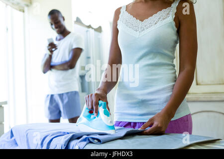 Sezione centrale della donna a stirare una camicia in cucina Foto Stock