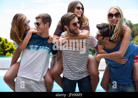 Tre uomini dando piggy bag a donne vicino alla piscina Foto Stock